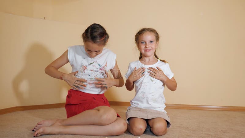 De kleine zusters die op vloer zitten en schilderen een t-shirt met hun handen