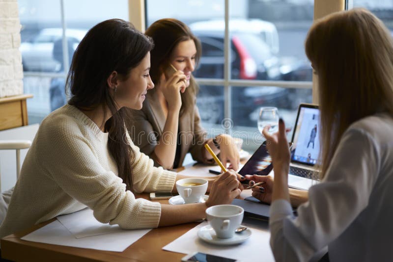 De kleren die van meisjesontwerpers verbonden met vrij draadloos Internet in koffiewinkel tijdens onderbreking samenwerken royalty-vrije stock foto's De kleren die van meisjesontwerpers verbonden met vrij draadloos Internet in koffiewinkel tijdens onderbreking samenwerken royalty-vrije stock foto's