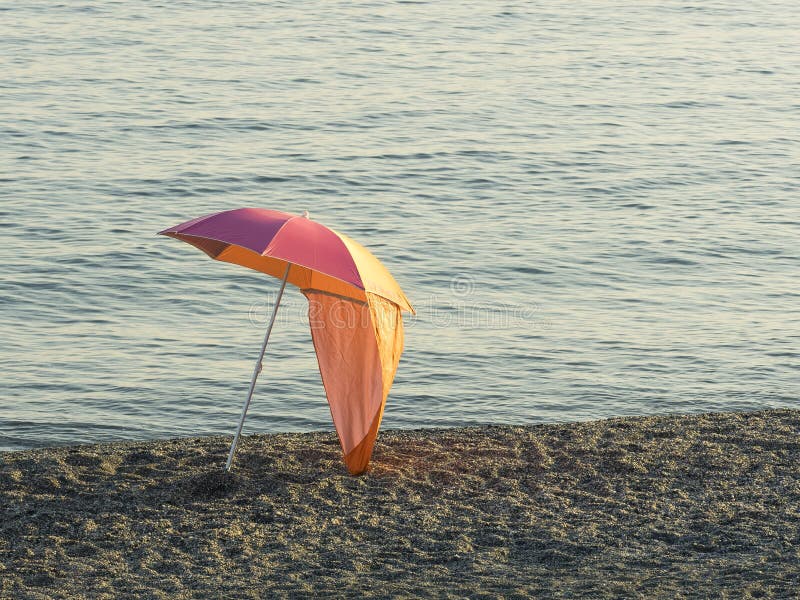 De kleurrijke die paraplu van het parasolstrand op een kiezelsteenstrand bij zonsondergang wordt geïsoleerd royalty-vrije stock afbeeldingen De kleurrijke die paraplu van het parasolstrand op een kiezelsteenstrand bij zonsondergang wordt geïsoleerd royalty-vrije stock afbeeldingen