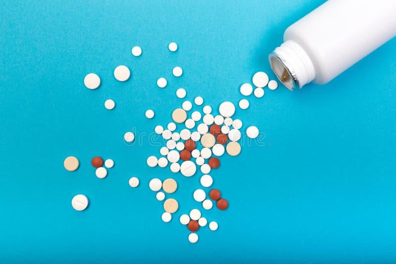 De kleurrijke verschillende tabletten morsten van een witte plastic fles op een lege blauwe achtergrond stock foto's De kleurrijke verschillende tabletten morsten van een witte plastic fles op een lege blauwe achtergrond stock foto's