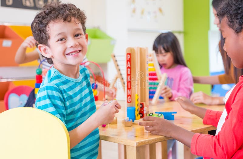 De kleuterschoolstudenten glimlachen wanneer het spelen van stuk speelgoed in speelkamer bij pres stock fotografie De kleuterschoolstudenten glimlachen wanneer het spelen van stuk speelgoed in speelkamer bij pres stock fotografie