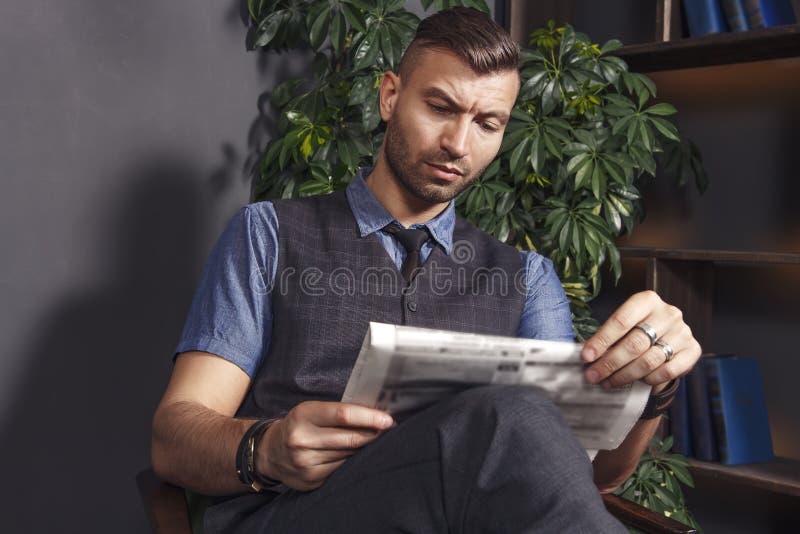 De knappe modieuze mens zit als voorzitter en leest recentste nieuws in krant zekere brutale zakenman in luxeflats royalty-vrije stock foto's De knappe modieuze mens zit als voorzitter en leest recentste nieuws in krant zekere brutale zakenman in luxeflats royalty-vrije stock foto's
