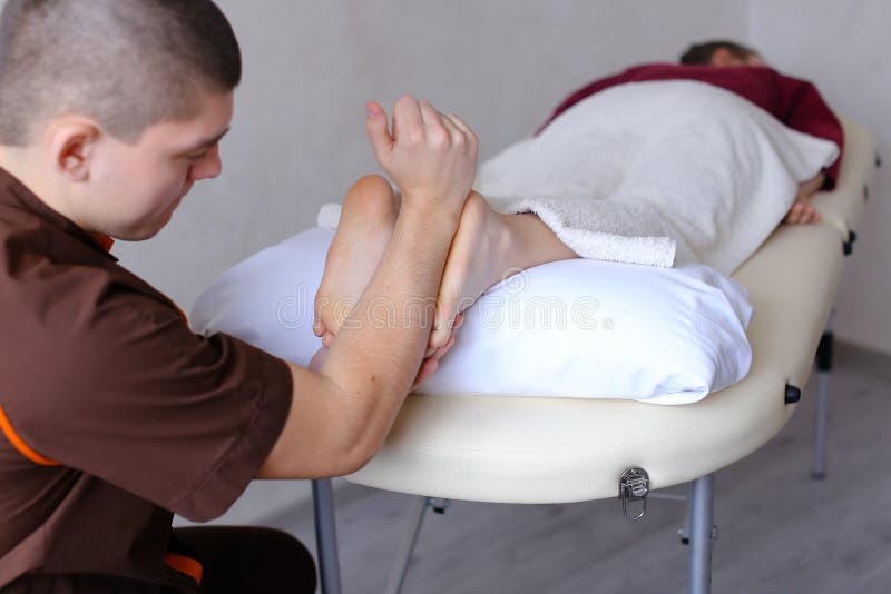 De knappe praktizerende masseur kneedt voeten van vrouwelijke cliënt, die Li