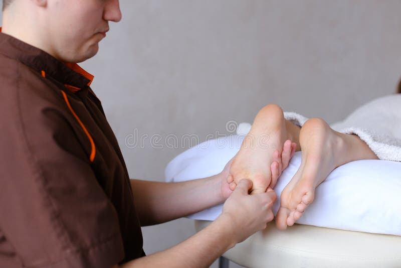 De knappe praktizerende masseur kneedt voeten van vrouwelijke cliënt, die Li