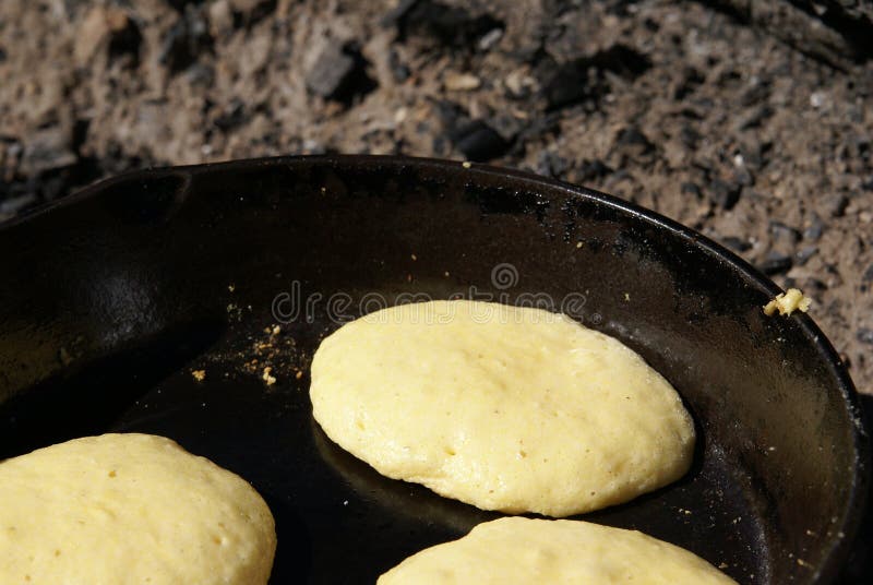 Cornmeal batter being cooked into pancakes in an iron skillet over an open fire. Cornmeal batter being cooked into pancakes in an iron skillet over an open fire