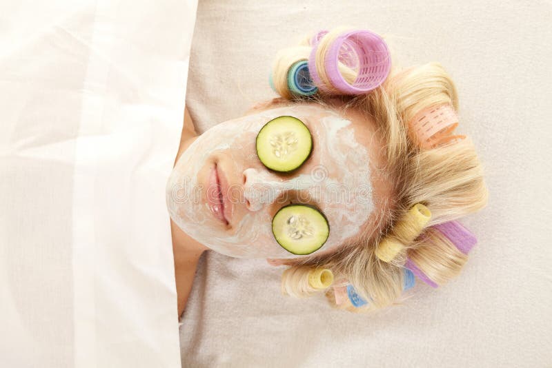 A woman is laying with curlers and a cream face mask. A woman is laying with curlers and a cream face mask.