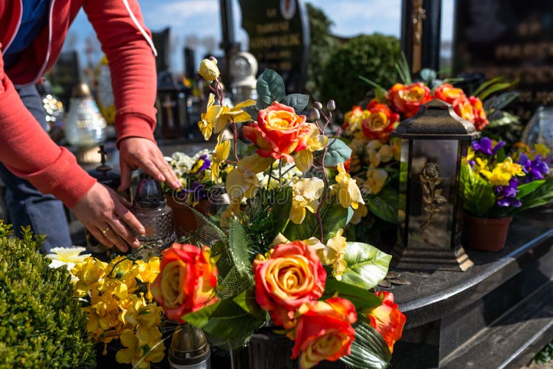De kunstbloemen en de kandelaars liggen op de grafsteen in de begraafplaats, zichtbare handen van een mens stock afbeeldingen De kunstbloemen en de kandelaars liggen op de grafsteen in de begraafplaats, zichtbare handen van een mens stock afbeeldingen