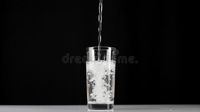 De l'eau douce pure est versée dans un verre transparent sur un fond noir. Concept de maison de séjour et à consommer de la nourri clips vidéos