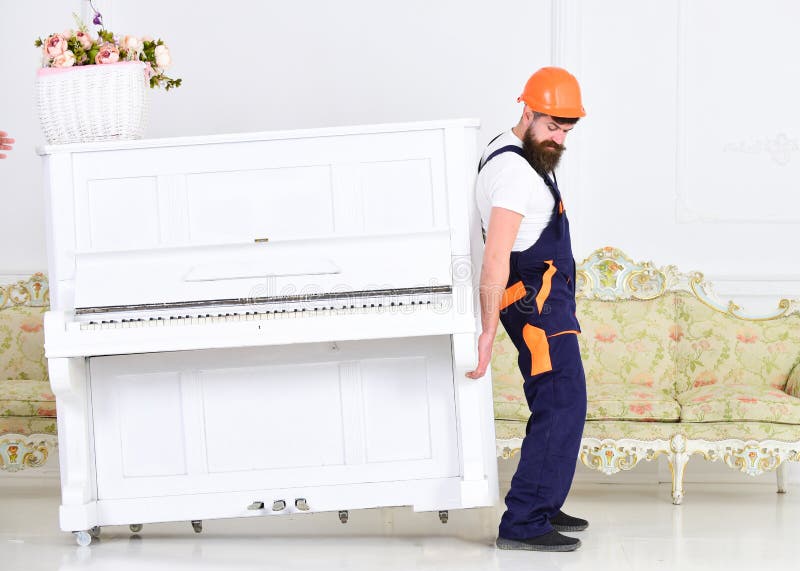 De lader beweegt pianoinstrument Zware ladingenconcept Mens met baard omhoog arbeider in helm en overallliften, inspanningen aan stock foto's De lader beweegt pianoinstrument Zware ladingenconcept Mens met baard omhoog arbeider in helm en overallliften, inspanningen aan stock foto's