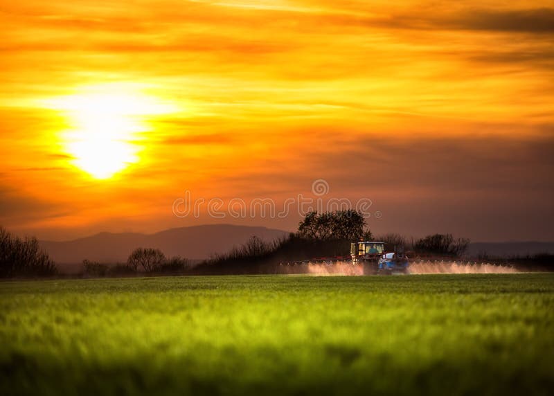 De landbouw van tractor die en bij zonsondergang ploegen bespuiten royalty-vrije stock foto De landbouw van tractor die en bij zonsondergang ploegen bespuiten royalty-vrije stock foto