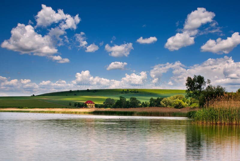 De landelijke het meer groene gebieden en de weilanden van het plattelandslandschap op achtergrond van blauwe hemel betrekken royalty-vrije stock afbeelding De landelijke het meer groene gebieden en de weilanden van het plattelandslandschap op achtergrond van blauwe hemel betrekken royalty-vrije stock afbeelding
