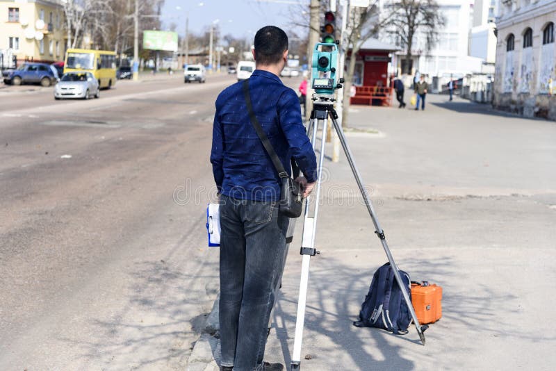 De landmeter van het ingenieursland maakt metingen op de straat van de stad van Chernigov, de Oekraïne stock foto's De landmeter van het ingenieursland maakt metingen op de straat van de stad van Chernigov, de Oekraïne stock foto's