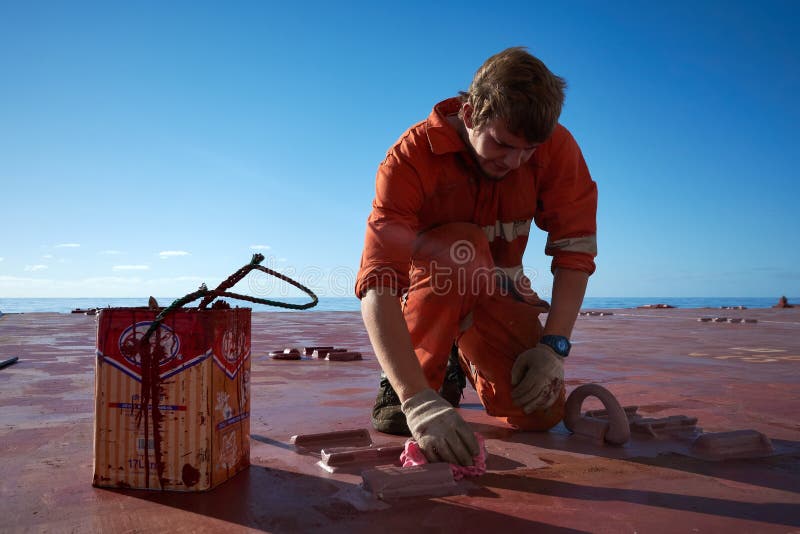 De leden die van de schepenbemanning broedseldekking in openlucht met heldere blauwe hemel op een achtergrond schilderen Het conc