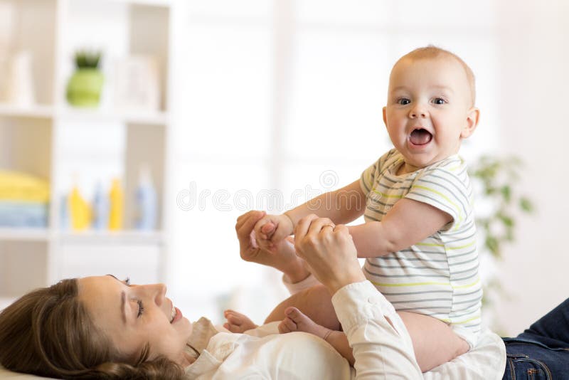 De leuke zitting die van de babyzoon op zijn gelukkig mamma op vloer thuis liggen royalty-vrije stock afbeeldingen De leuke zitting die van de babyzoon op zijn gelukkig mamma op vloer thuis liggen royalty-vrije stock afbeeldingen