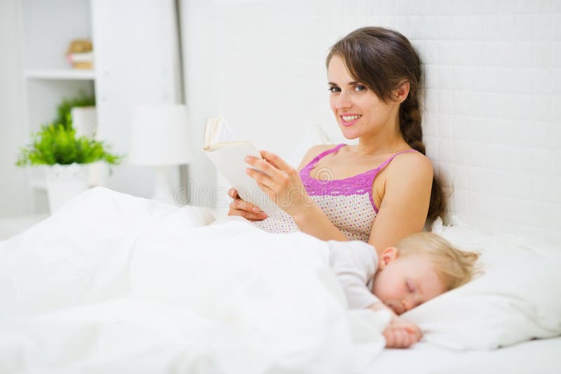 De lezing van de moeder in bed terwijl babyslaap royalty-vrije stock foto De lezing van de moeder in bed terwijl babyslaap royalty-vrije stock foto