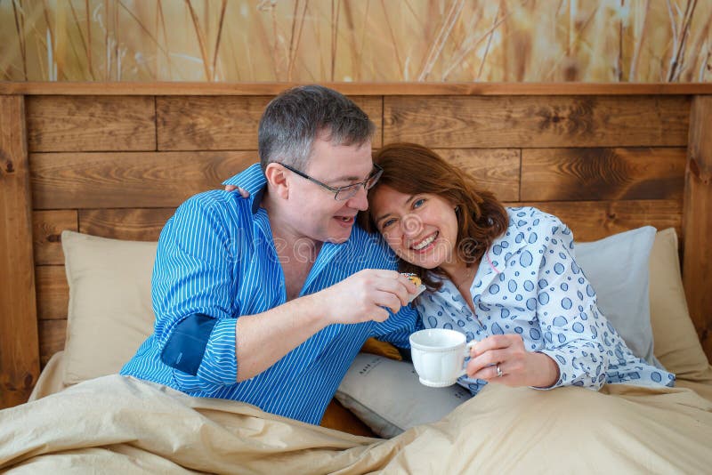 De lichte theekop met een hete drank De echtgenoot bracht zijn koffie van de vrouwenthee aan het bed stock foto De lichte theekop met een hete drank De echtgenoot bracht zijn koffie van de vrouwenthee aan het bed stock foto