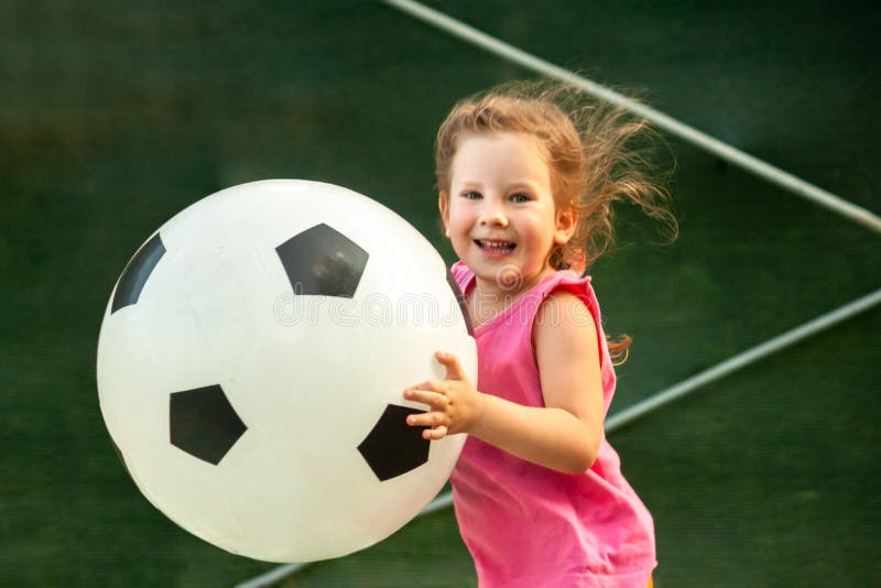 De looppas van weinig babymeisje met een reusachtige voetbalbal stock fotografie De looppas van weinig babymeisje met een reusachtige voetbalbal stock fotografie