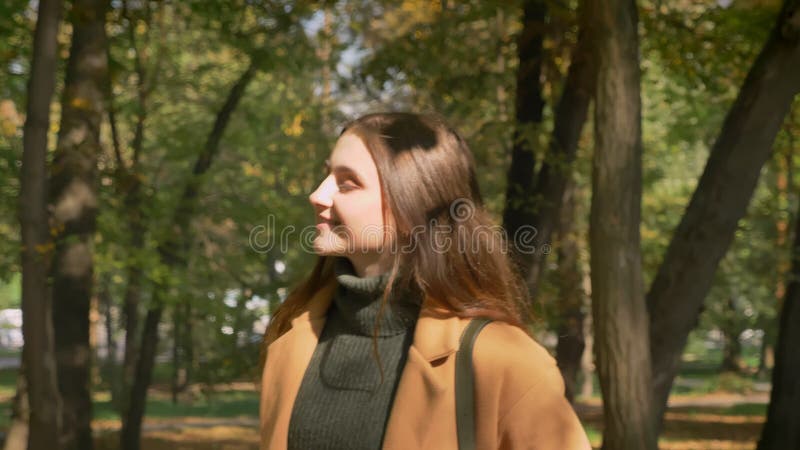 De lopende Kaukasische zwart-haired vrouw glimlacht en met sunlights op haar gezicht en ontspant op parkgebied, aard