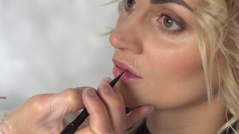 De make-upkunstenaar schildert de lippen van een jonge vrouw in een schoonheidssalon
