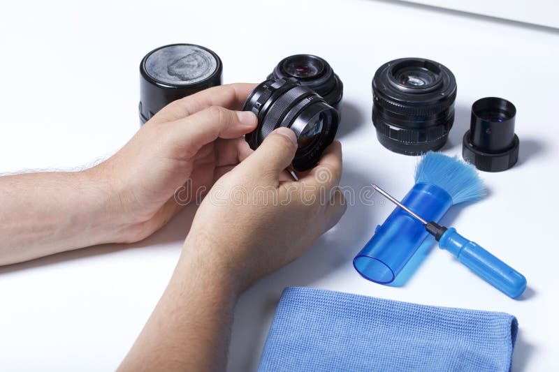 De man houdt een oude lens in zijn handen Dichtbij op de lijst lig andere uitstekende lenzen en apparaten voor reparatie en onder stock fotografie De man houdt een oude lens in zijn handen Dichtbij op de lijst lig andere uitstekende lenzen en apparaten voor reparatie en onder stock fotografie