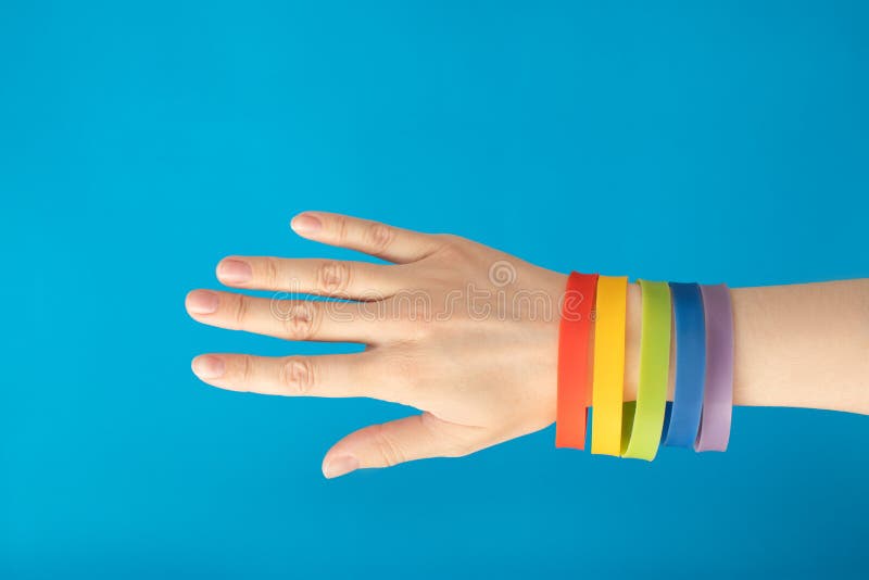 De manchetarmband van de regenboogvlag LGBT op vrouwelijke hand op blauwe achtergrond stock afbeelding De manchetarmband van de regenboogvlag LGBT op vrouwelijke hand op blauwe achtergrond stock afbeelding