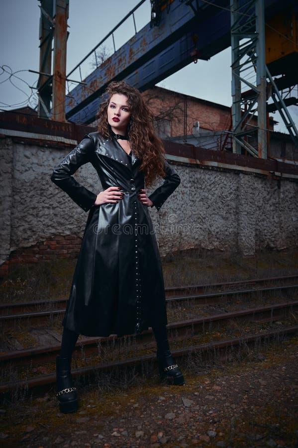 De manier schoot: portret van het mooie informele model van het gothmeisje in leerlaag die zich bij spoorweg industriezone bevind royalty-vrije stock afbeelding De manier schoot: portret van het mooie informele model van het gothmeisje in leerlaag die zich bij spoorweg industriezone bevind royalty-vrije stock afbeelding