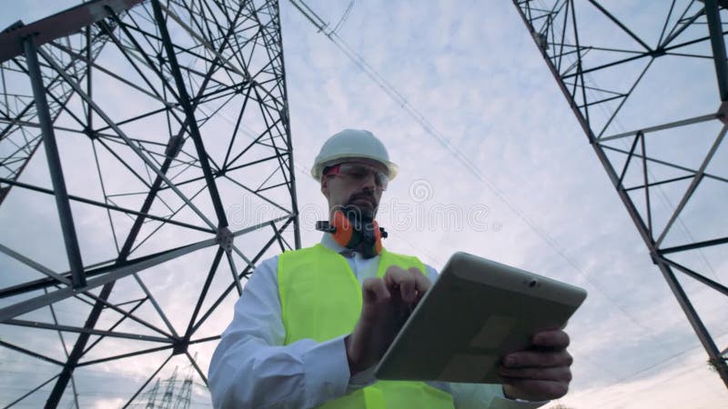 De mannelijke technicus doorbladert een computer terwijl het zijn dichtbij elektriciteitstorens stock videobeelden De mannelijke technicus doorbladert een computer terwijl het zijn dichtbij elektriciteitstorens stock videobeelden
