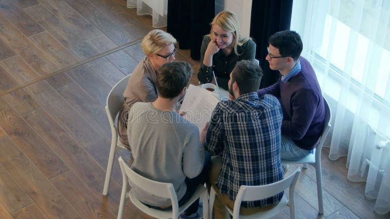 De mededeling van het team, groep van vijf mensen bespreekt iets met glimlach terwijl het zitten aan de bureaulijst