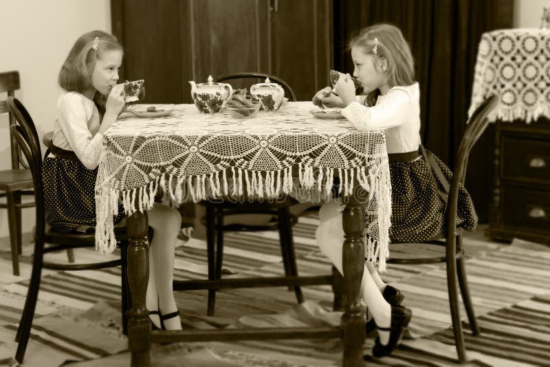 De meisjes brengt het drinken thee bij een antieke lijst samen met een kant tablecl stock foto De meisjes brengt het drinken thee bij een antieke lijst samen met een kant tablecl stock foto