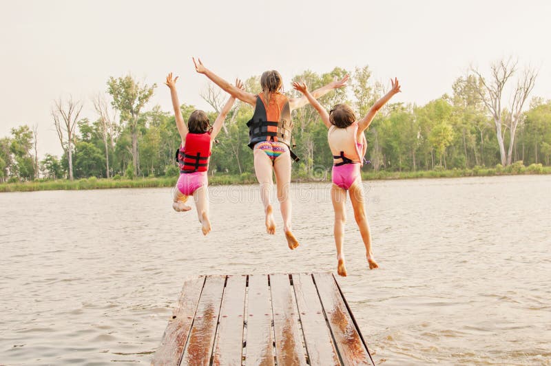 Three girls wear life jackets, and jump off boating dock into lake. Three girls wear life jackets, and jump off boating dock into lake