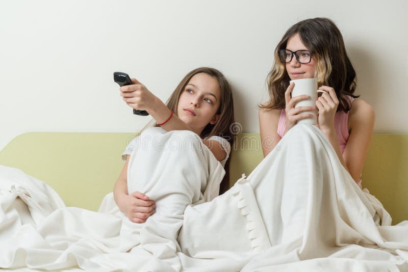 De meisjestieners zitten thuis in bed en het letten op TV royalty-vrije stock foto De meisjestieners zitten thuis in bed en het letten op TV royalty-vrije stock foto