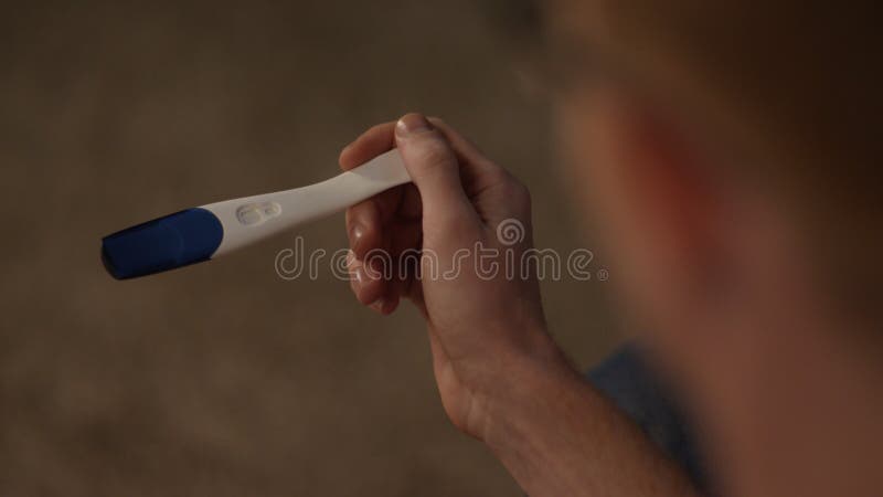 De mens bekijkt een zijaanzicht van de zwangerschapstest Positieve die zwangerschapstest door een verraste mens wordt gehouden De royalty-vrije stock foto De mens bekijkt een zijaanzicht van de zwangerschapstest Positieve die zwangerschapstest door een verraste mens wordt gehouden De royalty-vrije stock foto