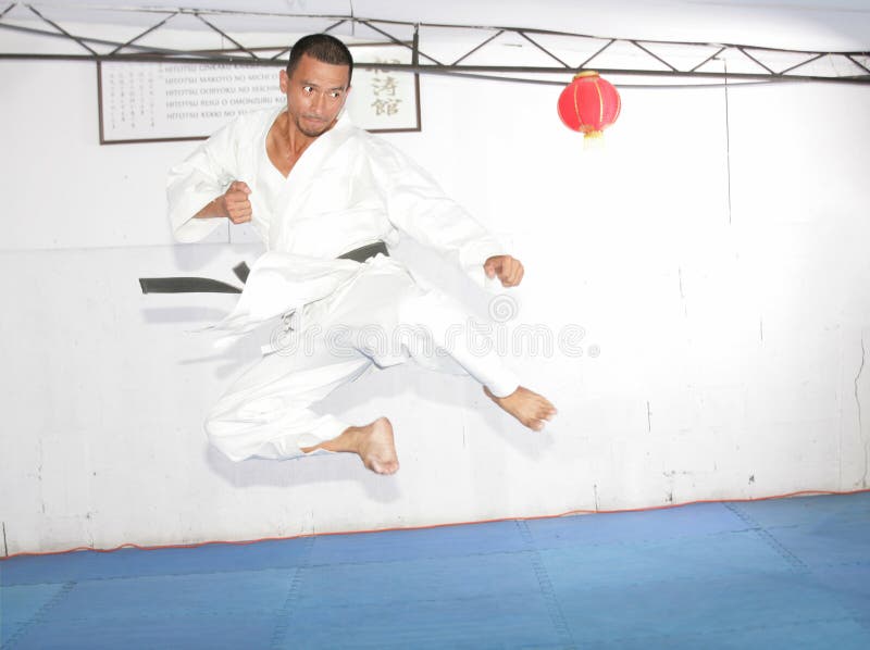 De mens die van de zwart bandkarate een hoge schop springen te geven stock foto De mens die van de zwart bandkarate een hoge schop springen te geven stock foto