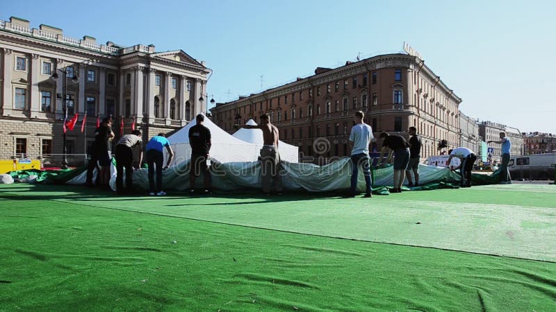 De mensen bouwen stadium voor gebeurtenis op straat De groep arbeiders houdt reusachtige groene tent Zon