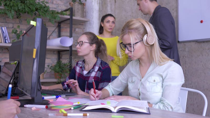 De mensen op het werk, jong team werken in modern bureau aan een meisje van het businessplan dan bekijken de camera en glimlachen