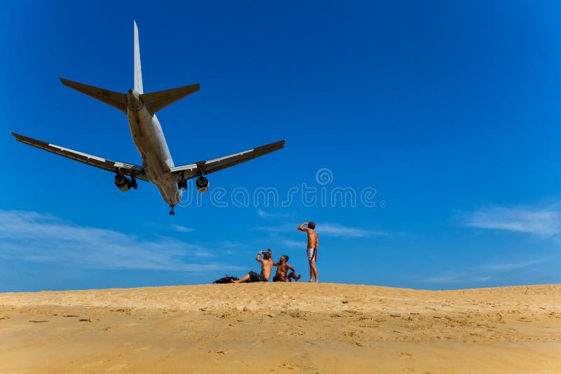 De mensen zitten op het strand en bekijken hen op een vliegtuig die over vliegen royalty-vrije stock foto De mensen zitten op het strand en bekijken hen op een vliegtuig die over vliegen royalty-vrije stock foto