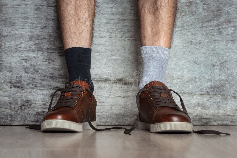 De mensenbenen in bruine leerschoenen en de verschillende sokken op een donkere achtergrond, sluiten omhoog Concept de vreemde id stock afbeeldingen De mensenbenen in bruine leerschoenen en de verschillende sokken op een donkere achtergrond, sluiten omhoog Concept de vreemde id stock afbeeldingen