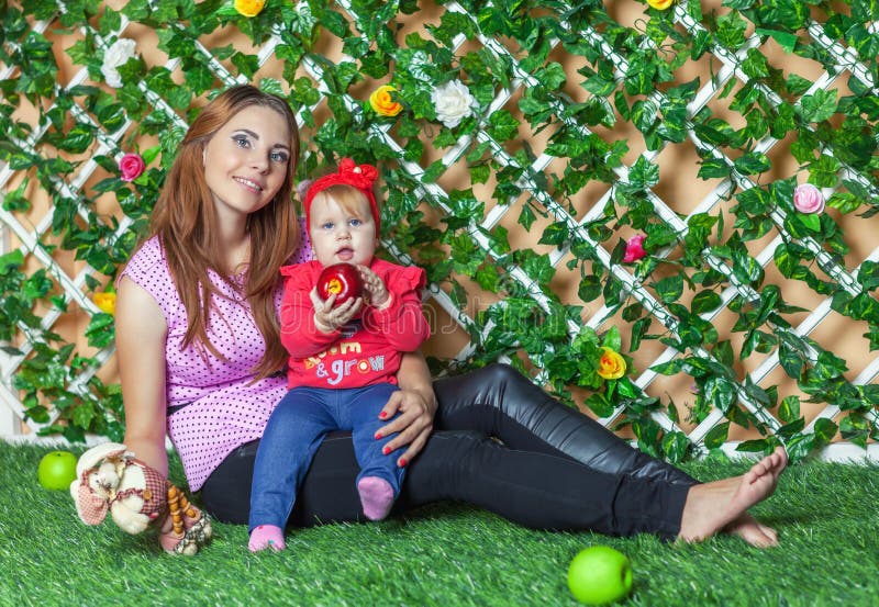 De moeder met baby op handzitting op het gras in de bloemtuin op een zonnige de zomerdag en eet appelen royalty-vrije stock foto De moeder met baby op handzitting op het gras in de bloemtuin op een zonnige de zomerdag en eet appelen royalty-vrije stock foto