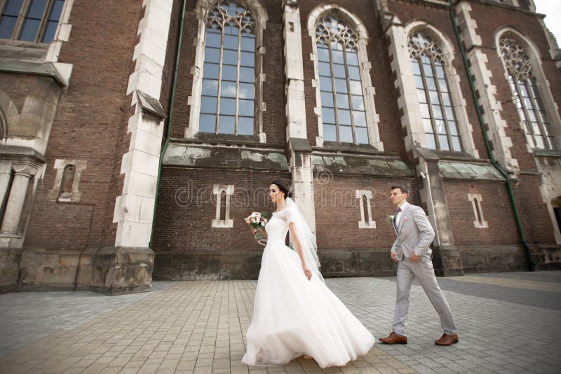De mooie gang van het jonggehuwdepaar dichtbij oude christelijke kerk stock foto De mooie gang van het jonggehuwdepaar dichtbij oude christelijke kerk stock foto
