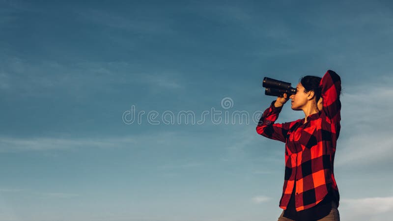 De mooie jonge meisjesreiziger kijkt door verrekijkers tegen een blauwe hemel met exemplaarruimte Het concept onderzoek, motivati royalty-vrije stock afbeelding De mooie jonge meisjesreiziger kijkt door verrekijkers tegen een blauwe hemel met exemplaarruimte Het concept onderzoek, motivati royalty-vrije stock afbeelding