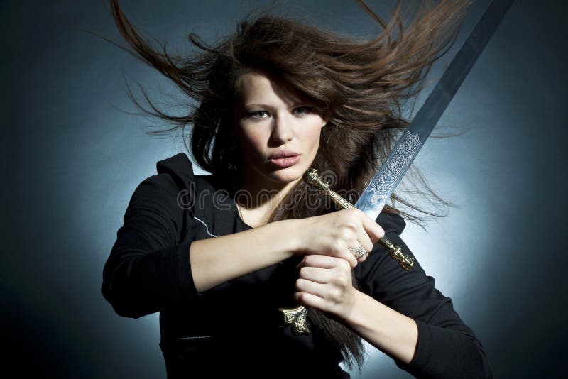 The beautiful young woman holds a sword in a hand. The beautiful young woman holds a sword in a hand