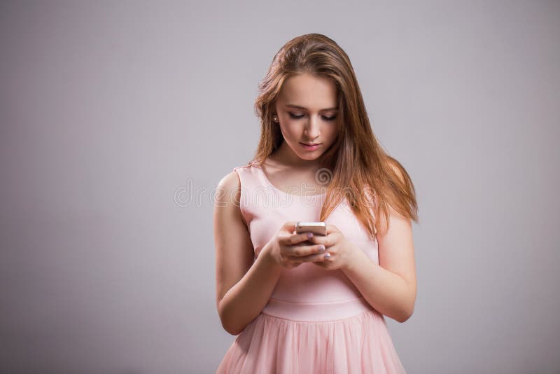 De mooie jonge vrouw draagt roze kleding en gebruikt smartphone op grijze achtergrond met exemplaarruimte royalty-vrije stock afbeelding De mooie jonge vrouw draagt roze kleding en gebruikt smartphone op grijze achtergrond met exemplaarruimte royalty-vrije stock afbeelding