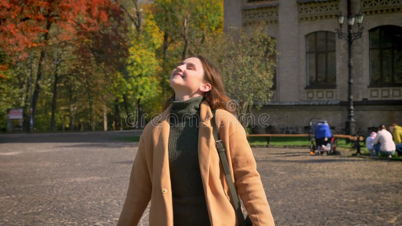 De mooie lopende Kaukasische vrouw maakt stappen op zonnige straat, zet cirkel aan en glimlacht met groot geluk