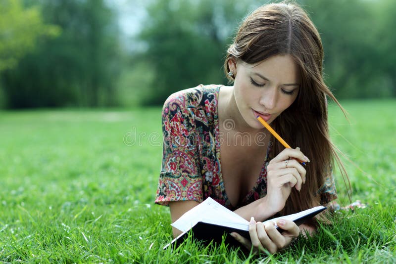 De mooie vrouw legt op een gras in park met een agenda in Ha stock fotografie De mooie vrouw legt op een gras in park met een agenda in Ha stock fotografie