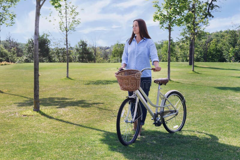 De mooie vrouw loopt in het park met fiets stock afbeeldingen