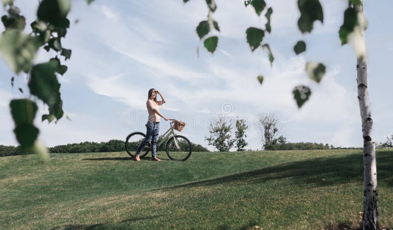 De mooie vrouw loopt in het park met fiets royalty-vrije stock afbeelding