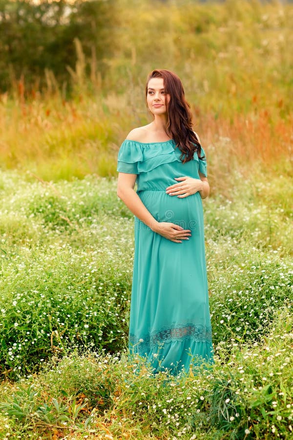 De mooie zwangere vrouw in een groene kleding bevindt zich in de wilgentuin op de zomerdag stock fotografie De mooie zwangere vrouw in een groene kleding bevindt zich in de wilgentuin op de zomerdag stock fotografie