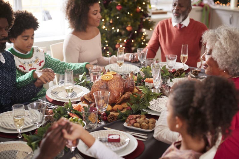 De multigeneratie mengde de zitting van de rasfamilie bij de handen van de de lijstholding van het Kerstmisdiner en het zeggen va stock fotografie De multigeneratie mengde de zitting van de rasfamilie bij de handen van de de lijstholding van het Kerstmisdiner en het zeggen va stock fotografie