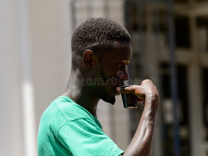 De niet geïdentificeerde Senegalese mens houdt een plastic kop in het centrum o stock foto De niet geïdentificeerde Senegalese mens houdt een plastic kop in het centrum o stock foto