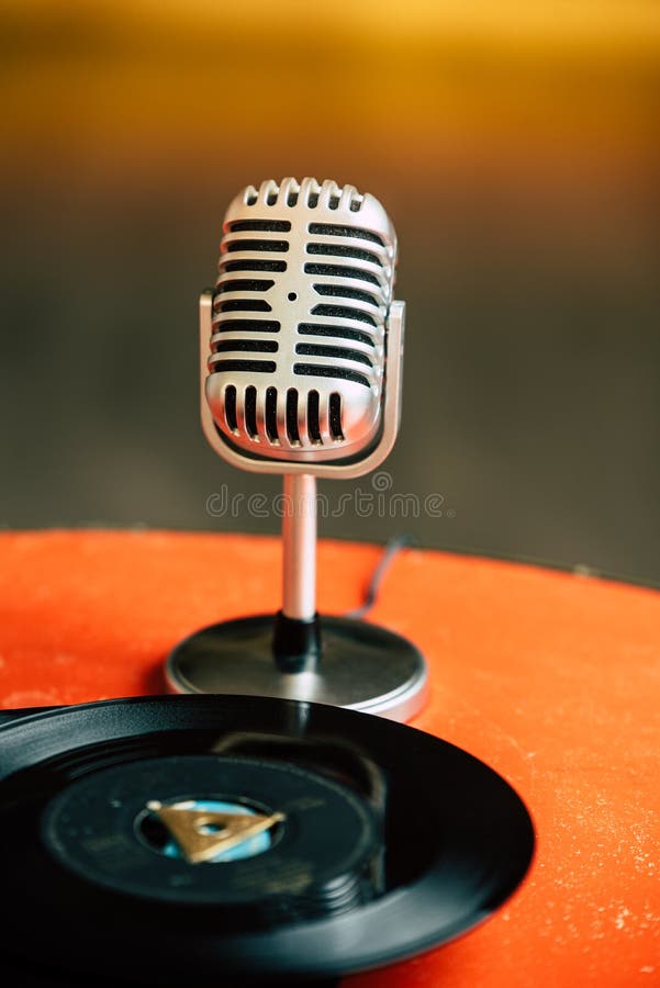 De nuevo a 50s - imagen nostálgica de un micrófono de los años 50 que se coloca en una tabla anaranjada vieja con los viejos disc imagen de archivo De nuevo a 50s - imagen nostálgica de un micrófono de los años 50 que se coloca en una tabla anaranjada vieja con los viejos disc imagen de archivo
